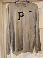 Grey long sleeve Nike Pittsburgh Pirates shirt with a black 'P' logo and Nike swoosh on the chest, hanging on a hanger