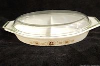 Side angle photo of the Pyrex Town & Country 1.5 quart divided casserole with glass lid, showing outer decorative motifs and handles.