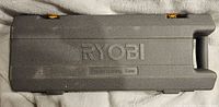 Closed view of the grey plastic Ryobi case with yellow latches for storing the saw