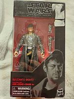Front view of Star Wars The Black Series DJ action figure in original packaging, showing the figure, two blasters, and portrait of DJ on box.