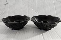 Pair of black Indiana Glass Tiara candleholders side by side on a white surface with visible floral scalloped edges and embossed details.