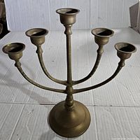 Full view of brass menorah with five candle holders on a white background.