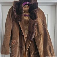 Full front view of the brown corduroy coat with faux fur collar and flap pockets, showing the button closure and details of the fabric texture.