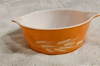 Side view of the vintage Pyrex Autumn Harvest Wheat bowl showing orange exterior with white wheat pattern and white interior with pouring spout.