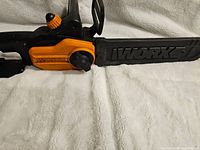 Close-up of WORX branded cutting bar and orange adjustment knob on the chainsaw.