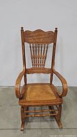 Front view of the oak wood antique rocking chair showing carved backrest and cane seat.