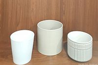Three ceramic planters displayed side by side on wooden surface; plain white, cream-colored etched, and grey/white etched.