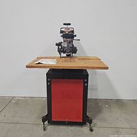 Full view of Craftsman radial saw mounted on a wooden tabletop and mobile metal stand with red front panel and caster wheels.