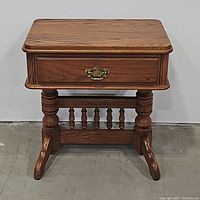 Front view of solid wood nightstand with drawer and brass handle showing decorative footed legs and spindle detailing.