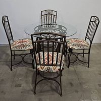 View of the full dining set including round glass table and four metal chairs with patterned upholstery