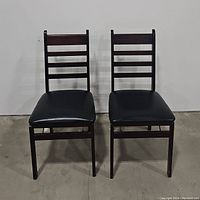 Pair of folding chairs with leather seats and dark wooden frames, front view.
