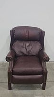 Front view of burgundy leather recliner chair showing padded back and arms, nailhead trim, wooden legs.