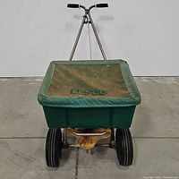 Front view of the green Lesco spreader with cover showing two wheels and hopper with cover
