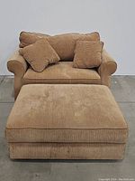 Front view of beige corduroy loveseat sleeper with two throw pillows and large matching ottoman in front.