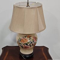 Full view of the porcelain jar table lamp with floral decoration, beige shade, and wooden base