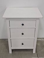 Front view of white nightstand with three drawers closed.