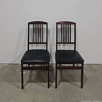 Pair of wooden folding chairs with slatted backs and black cushioned seats, viewed from the front.