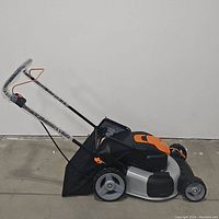 Side view of the Worx Nitro electric lawn mower showing its silver and black metal body with orange accents and rear grass collection bag attached.