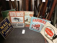 Group of six vintage metal advertising signs, showing various themes such as tobacco, auto racing, farming, hunting, and beverages.