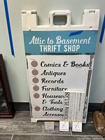 Front view of the plastic sandwich board sign showing the printed thrift shop advertisement