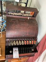 Oblique view of cash register open showing wooden top, key hole and front keys.