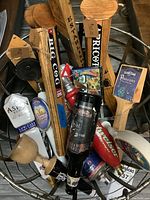 Top view of multiple beer tap handles arranged in a basket showing various brands and designs including wooden handles and bottle shaped handles.