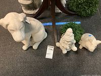 Three concrete statues including a large dog, an elf figure, and a pig with faux greenery in background.