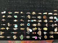 Top-down view of multiple costume rings arranged on black foam display pad, showing variety of styles and colors.