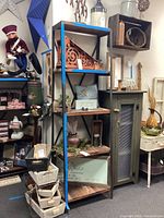 Front view of the shelving unit displaying four wood shelves in a black metal frame with blue tape on one side, surrounded by various decorative items (not included).