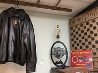 Brandini black leather jacket hung on hanger next to Harley-Davidson lamp and sign, and rustic checkerboard panel