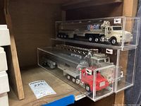 Two Mobil model tanker trucks with white and red cabs in clear display cases on a shelf.