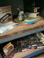 Figurine sitting on motorcycle, and two NASCAR Matchbox cars in original boxes below shelf