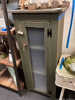 Front view of the green wooden pie safe with a wire mesh door closed, showing the wooden latch and black hinges.