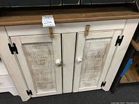 Front view of primitive style painted wood cabinet base, showing two doors with distressed panels, white knobs, and black metal hinges.