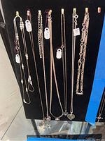 Photo showing seven sterling silver necklaces hanging on hooks, featuring various pendants including hearts, stars, and peace sign hand.