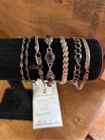 Seven sterling silver bracelets displayed on black stand, varied styles including stone-set and rope chains.