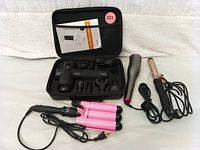 Photo of all items laid out including massage gun with attachments in case, pink triple-barrel curling iron, hot air brush, and rose gold curling iron.