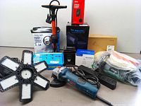 Photo overview showing Bosch grinder, LED work light, boxed clamp light, bug zapper, air screwdriver, power strip and other tools.