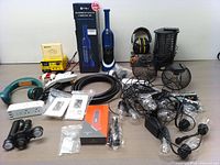 Full view of all items in lot including handheld vacuum, battery charger, string lights, extension cords, mesh baskets, ear protection, and other household accessories arranged on table.