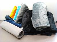 All heated blankets and heating pads rolled and stacked on a white background showing the variety of colors and sizes.