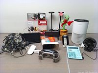 Photo showing various items including cables, USB fan, calculator, cactus figurine, digital scale, and small lights alongside smart air purifier and other electronics on a wooden table.