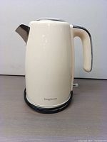 Side view of cream colored Longdeem electric kettle showing smooth body and chrome spout, with brand name visible.