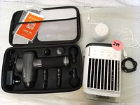 Open zippered black case showing a gray massage gun with five different massage heads and power adapter.