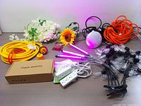 Full view of all items including extension cord, power inverter box, LED grow light tubes, string lights, power strips, alarm clock, and decorative flowers