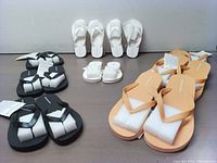 Top view of the sandals showing three pairs each of white, black, and peach Amazon Basics outdoor sandals arranged in rows, with packaging tags visible.