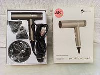 Opened retail box showing metallic grey hair dryer, 2 black nozzle attachments, diffuser, and power cord