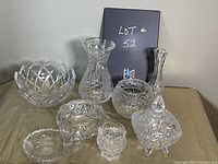 Image showing all 8 crystal pieces displayed on a beige cloth, includes various shaped vases and bowls with cut crystal designs.