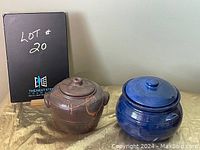 Photo shows two bean pots side by side with lids on, set on a table with a display board.