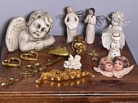 Angel figurines in various styles and materials placed on a wooden surface against gray wall.