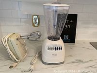 Osterizer blender and Phillips hand mixer placed side by side on countertop showing overall condition and items included.